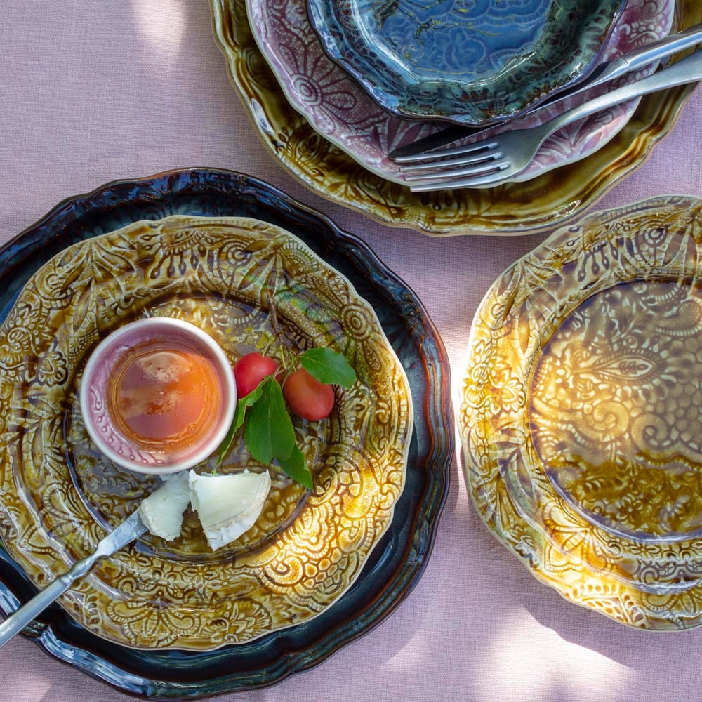 Sthål keramikk – dekorative tallerkener i ulike farger på rosa linduk, med ost, plommer og kopp