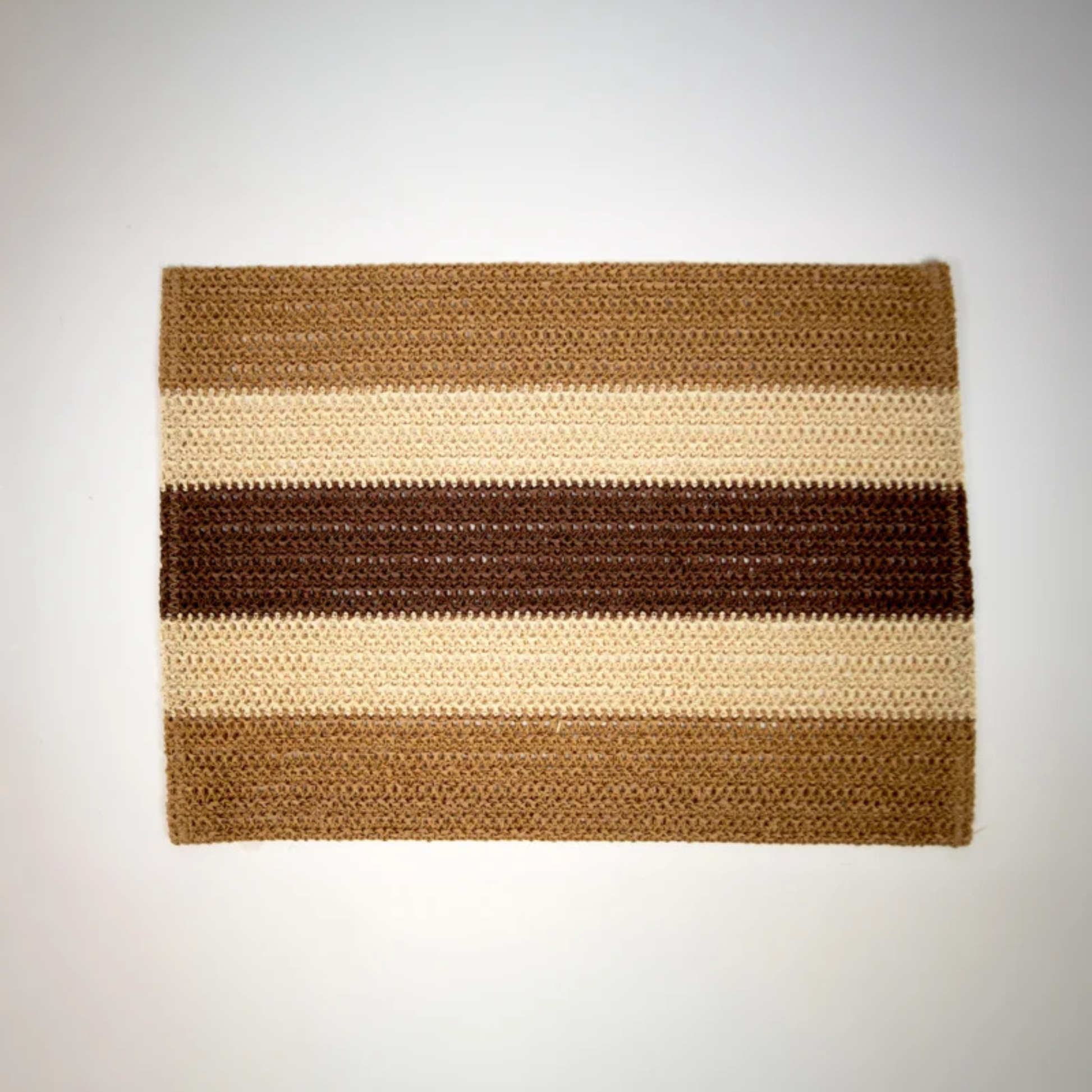 Bordbrikke i papirraffia med håndflettet struktur i jordnære nyanser av beige, karamell og brun.