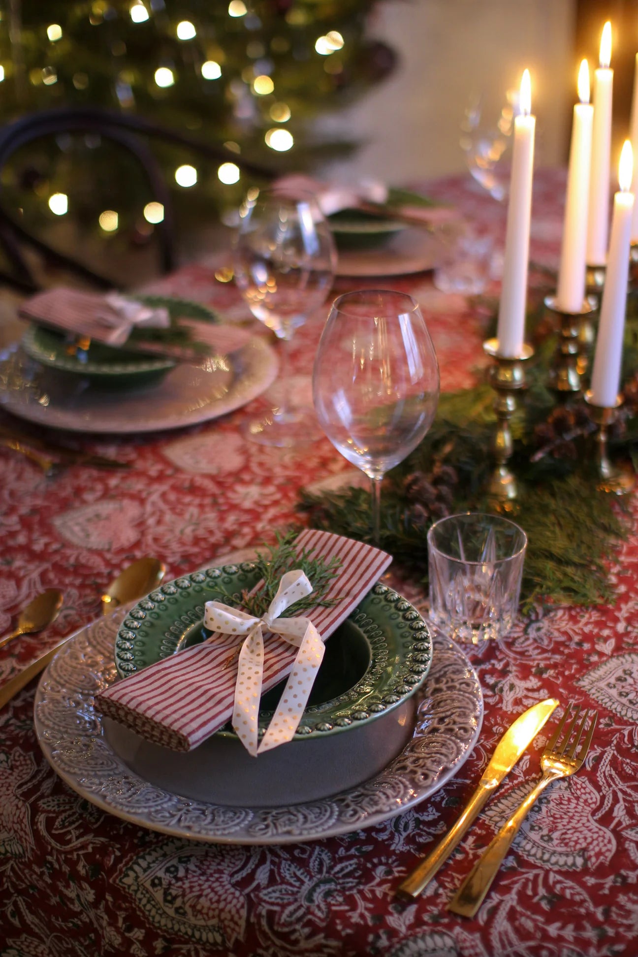 Dekket julebord med håndtrykket rød orientalsk duk, levende lys og julepynt i klassisk stil.