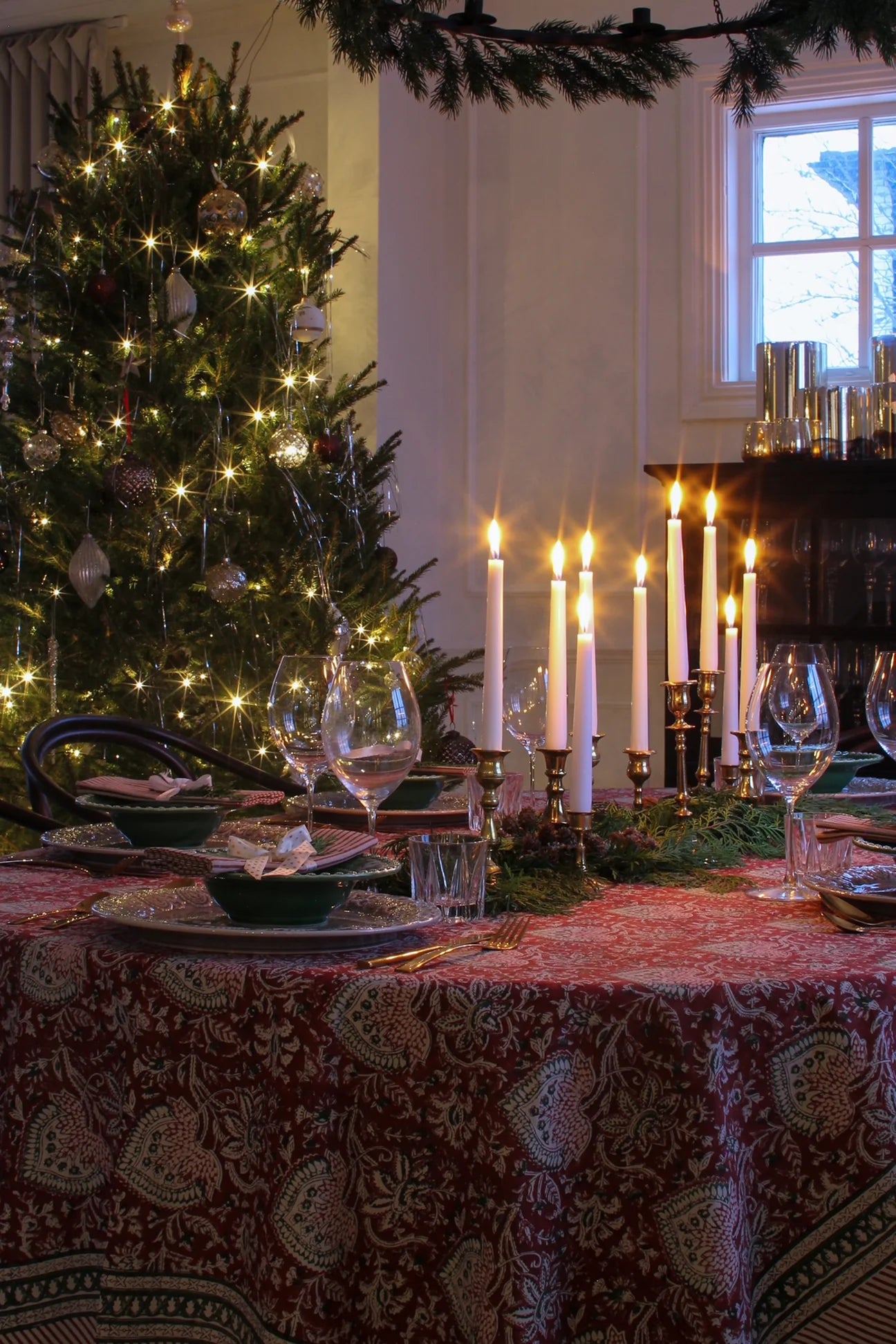 Detaljbilde av julebord med orientalsk duk i rødt og grønne tallerkener, omgitt av tente lys.