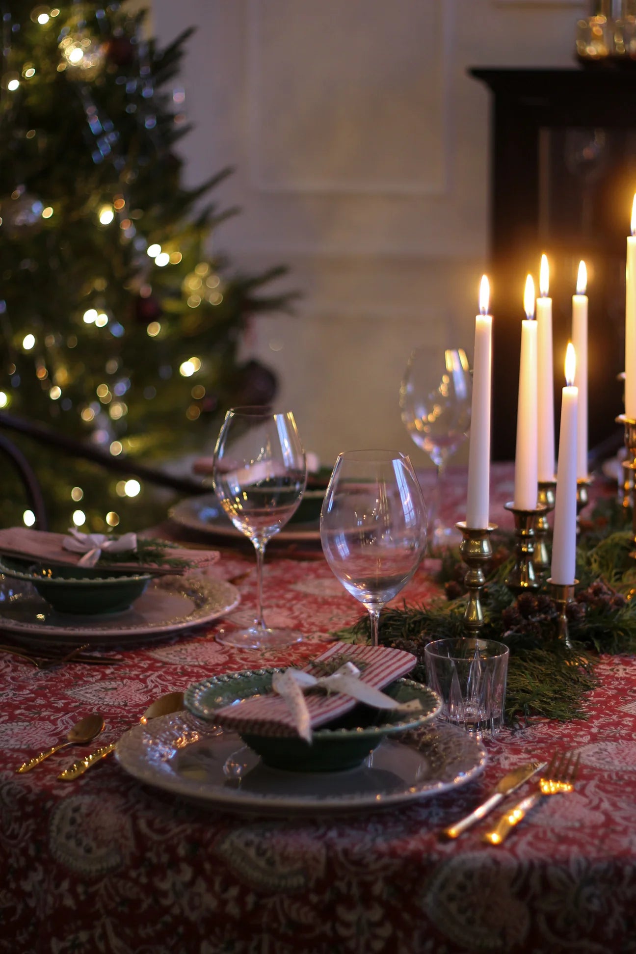 Stemningsfull julemiddag med rød orientalsk duk, tente lys og juletre i bakgrunnen.